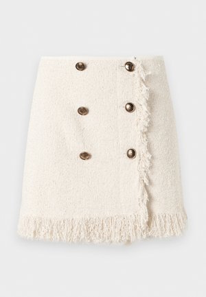 Mini-jupe crème texturée ornée de six boutons décoratifs dorés et bordée de franges sur le devant et l'ourlet.