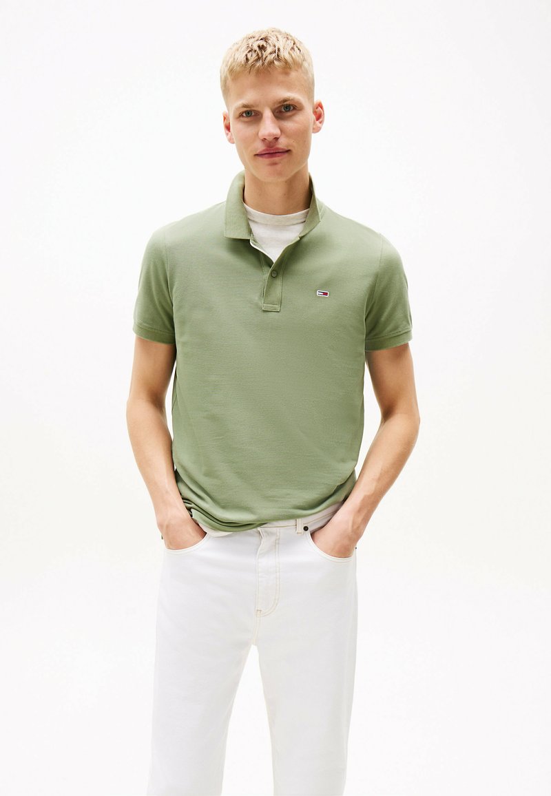 Camisa polo verde claro con cuello y mangas cortas, hecha de una tela suave y texturada. Presenta un pequeño logo en el pecho. Combinada con pantalones blancos.