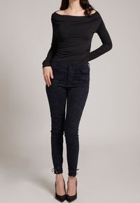 Černý top bez ramínek v kombinaci s tmavě modrými vzorovanými skinny džíny s úzkým střihem a zavazováním u kotníků, doplněný černými podpatky.