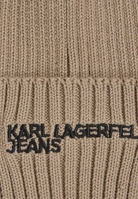 Beige kötött pulóver vertikális bordázással, az alján fekete hímzett "KARL LAGERFELD JEANS" logóval.
