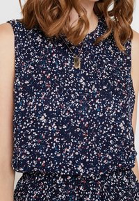Marineblaues ärmelloses Oberteil mit einem gesprenkelten Muster in Weiß, Rot und Blau. Leichter, strukturierter Stoff; runder Halsausschnitt; geraffte Taillendetail.