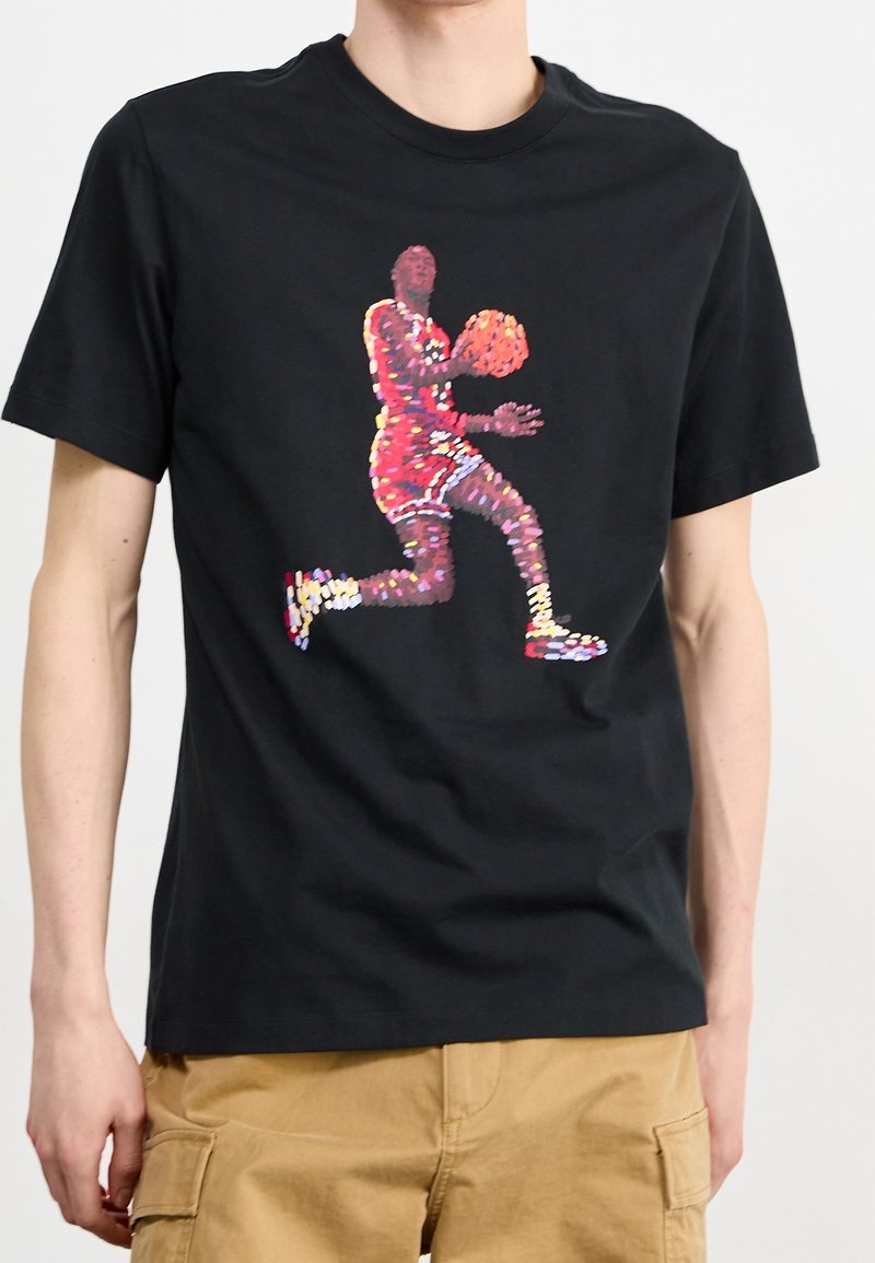 T-shirt en coton noir avec un impression graphique colorée d'un joueur de basketball en mouvement, présentant des rouges, des jaunes et des violets vifs.