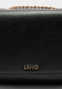 Črna usnjena torbica s teksturo, z zlatim ročajem iz verige in zlatim logotipom "LIU·JO" na središnji sprednji strani.