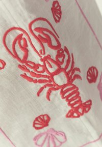 Homard rouge brodé et coquillages sur tissu blanc, avec bordure brodée rose.
