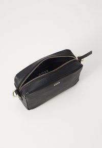 Borsa a tracolla nera in pelle con forma rettangolare, dettaglio della zip dorata e logo impresso sul lato. Interno foderato.