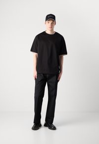 Camiseta negra de manga corta con ribete en contraste, combinada con pantalones negros y zapatos negros. Una gorra negra con un logo completa el look.