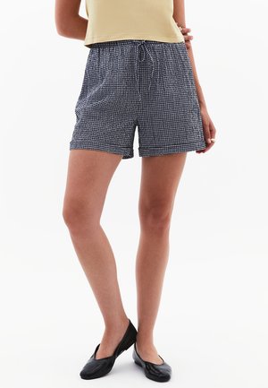 Shorts à carreaux navy et blancs avec une taille élastique et un cordon de serrage. Tissu léger, longueur genou, associés avec des ballerines noires.