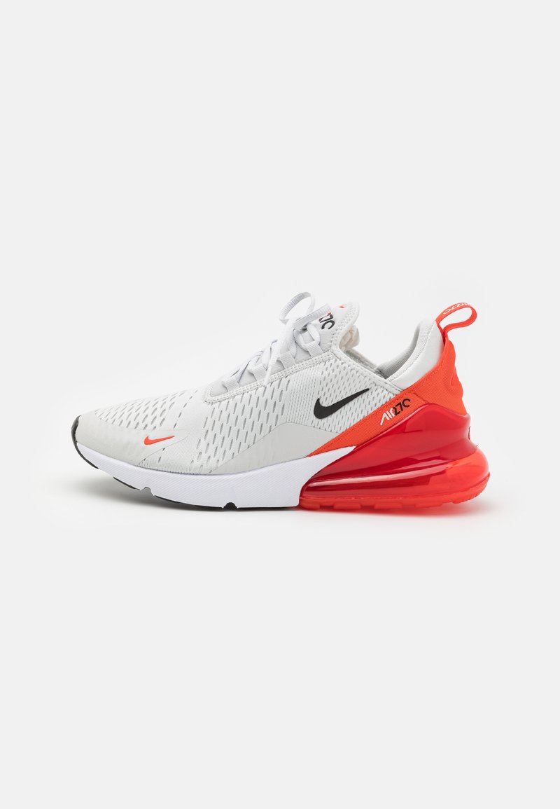 Fehér sportcipő légáteresztő hálós felsőrésszel, fekete Nike logóval, narancssárga sarokdíszítéssel és látható légpárnázással a talpban.