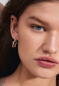 Orecchini color oro con un design ondulato, caratterizzati da una superficie texturizzata e accenti glitterati. Forma minimalista elegante, adatta a varie occasioni.