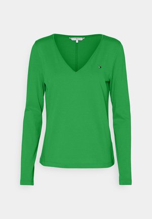 Zielona koszulka z długim rękawem i dekoltem w serek z małym logo Tommy Hilfiger na lewej piersi, przedstawiona na białym tle.