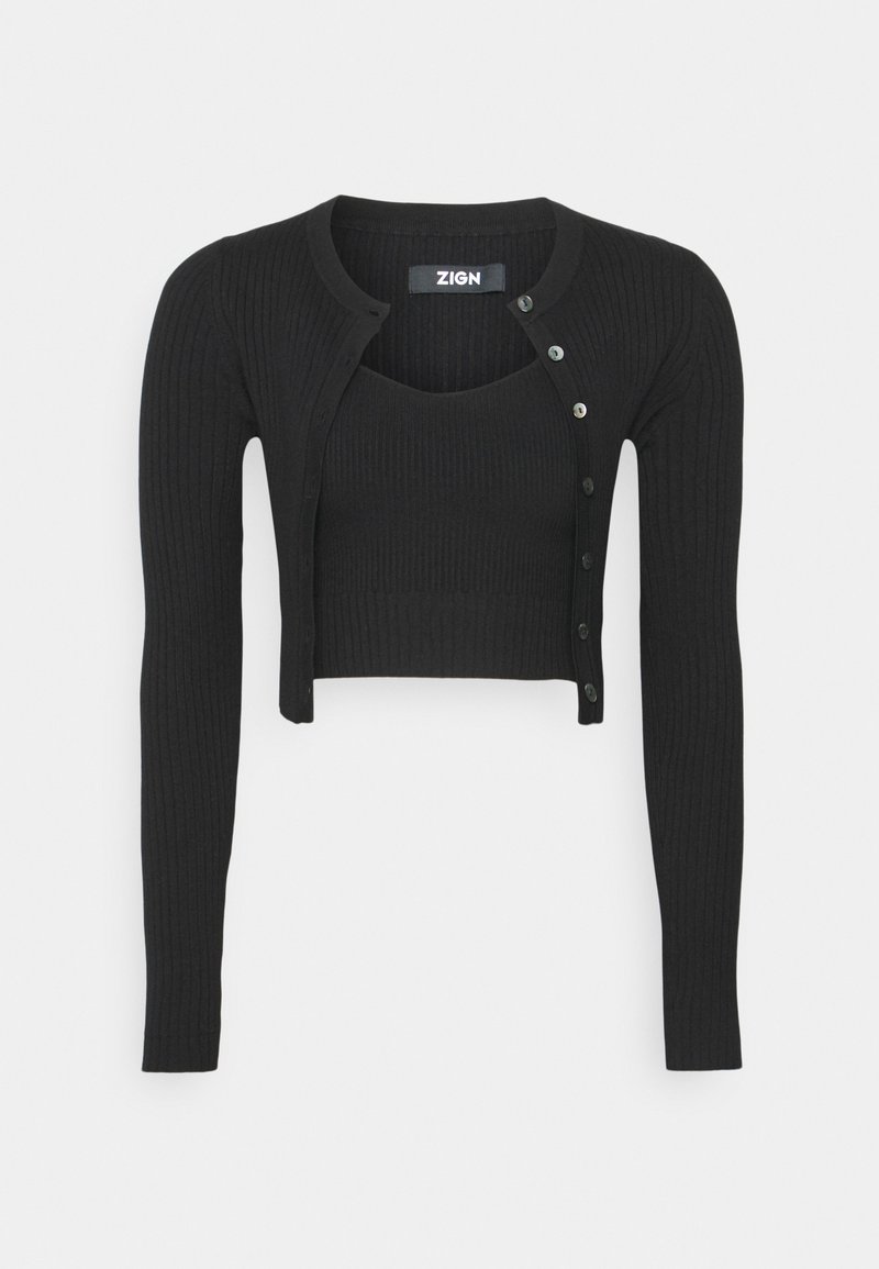 Ensemble deux pièces en maille côtelée noire avec cardigan à manches longues cropped et top court sans manches assorti, partiellement boutonné sur un fond clair.