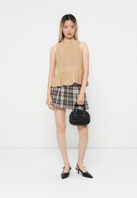 Beige microsude peplum-top med flared nederdel, parret med en ternet mini-nederdel. Sort struktureret håndtaske og spidse sorte hæle.