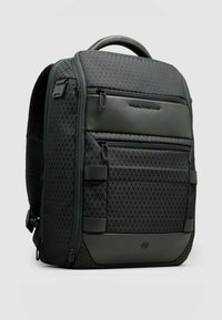 Mochila verde oscuro hecha de tela texturizada con un patrón geométrico, que cuenta con múltiples bolsillos con cremallera y un asa resistente.