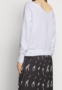 Maglione lavorato a maglia di un leggero lavanda, con design a V sulla schiena, polsini e orlo a coste. Abbinato a una gonna plissettata nera con testo bianco.