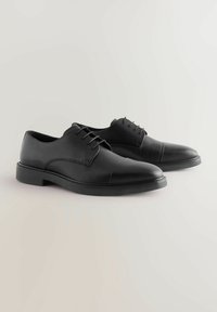 Zapatos de vestir de cuero negro con punta redonda, diseño de cordones, textura suave y acentos de costura en contraste a lo largo de la suela.