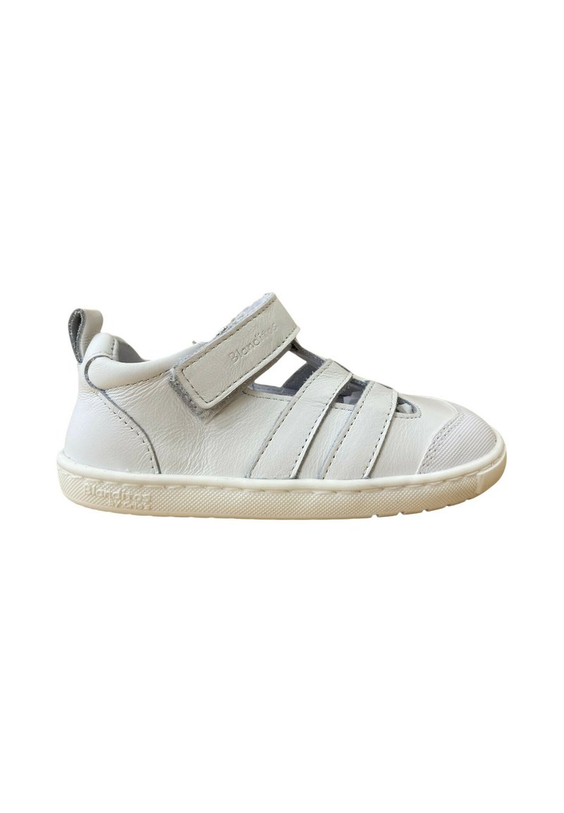 Zapato infantil de cuero blanco con puntera redonda, tira de Velcro y diseño recortado. Suela de goma con agarre texturizado, con acentos minimalistas.