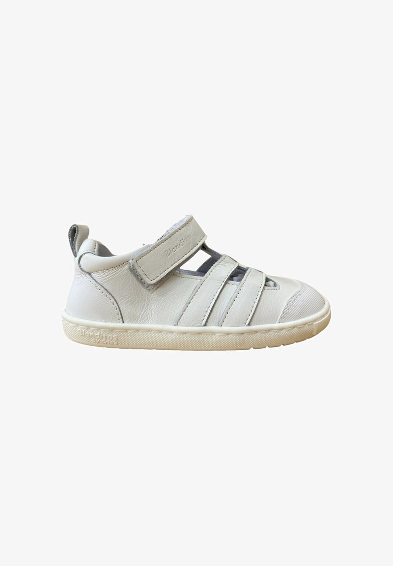 Zapato infantil de cuero blanco con puntera redonda, tira de Velcro y diseño recortado. Suela de goma con agarre texturizado, con acentos minimalistas.