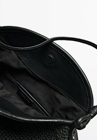 Borsa nera con rifiniture in pelle e texture intrecciata. L'apertura superiore rivela un interno in tessuto nero morbido con una tasca a soffietto e dettagli di chiusura.