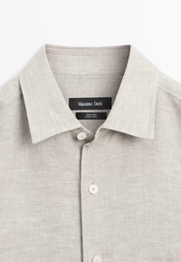 Chemise en lin beige clair avec col ouvert et boutons blancs, étiquetée Massimo Dutti, fabriquée en Chine, vue de face.
