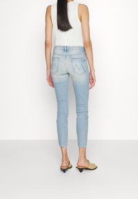 Jeans skinny de color azul claro con un acabado desgastado y dobladillo deshilachado. La parte trasera cuenta con dos bolsillos con un diseño en zigzag. Combinados con mules de tacón beige.