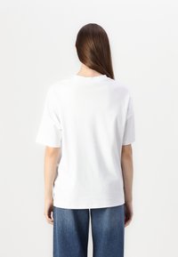 T-shirt bianca in cotone con collo rotondo e maniche corte, mostrata dal retro. Abbinata a pantaloni in denim larghi.