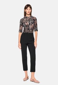 Schwarzes florales Oberteil mit kurzen Ärmeln, kombiniert mit maßgeschneiderten schwarzen Hosen und hellrosa Ballettschuhen. Klare Linien und strukturierte Muster.