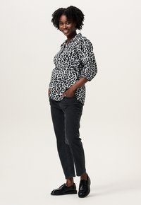 Zwart-witte blouse met luipaardprint en pofmouwen, gedragen met donkergrijze jeans en zwarte loafers; model staat met handen in de zakken.