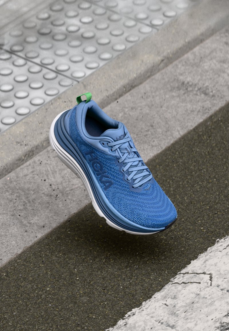 Chaussure de sport bleue avec tige en maille texturée, dotée d'une semelle intermédiaire blanche et d'une languette verte. Conçue pour le confort et la stabilité.