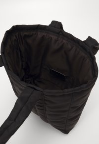 Czarna pikowana torba na ramię z materiałowymi uchwytami, otwarta na górze, z widoczną małą kieszonką w środku, na jednolitym tle.