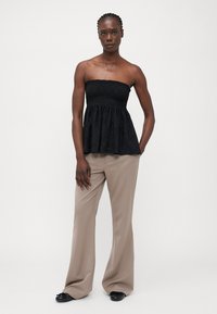 Zwarte strapless top met een smock-borsten, peplumdesign en gestructureerde stof, gecombineerd met beige wijde broek en zwarte platte schoenen.