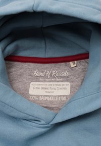 Blå bomulls hoodie med grå insida. Har en röd detalj runt halsen och etiketter som anger "100% bomull" och "Global Organic Textile Standard."