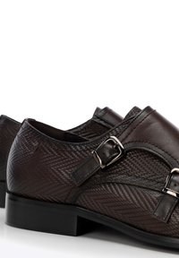 Los zapatos de cuero marrón presentan un patrón texturizado, acentos de doble hebilla, una punta redondeada y una suela negra lisa.