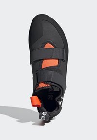 Schwarzer Kletterschuh mit synthetischem Obermaterial, orangefarbener Netzplatte, zwei schwarzen Klettverschlüssen und einem kontrastierenden orangefarbenen Zugband an der Ferse.