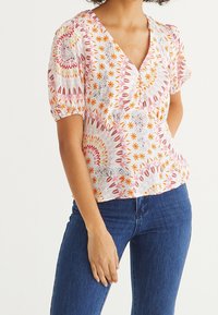 Blusa a maniche corte in tessuto leggero, con un motivo floreale caratterizzato da accenti in rosa, arancione e giallo su uno sfondo bianco.