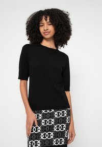 Top preto de malha com mangas curtas e gola redonda, apresentando uma textura lisa. Combinado com uma saia lápis preta e branca com padrão.