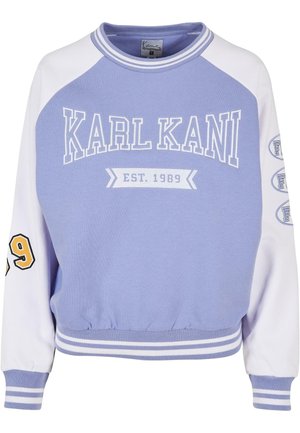 Vijoličen pulover s toplimi belimi raglan rokavi, ki vsebuje 'KARL KANI EST. 1989' v belih in rumenih poudarkih, z rebrastim ovratnikom in robom.