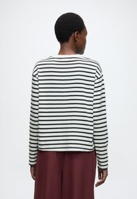 Hosszú ujjú felső fekete-fehér vízszintes csíkokkal, kerek nyakkivágással és laza szabással, bordó, bő szárú nadrággal kombinálva.