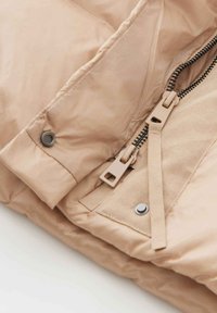 Light beige puffer jacket with a smooth, shiny texture. Features a two-way zipper, snap buttons, and contrasting black zipper teeth.