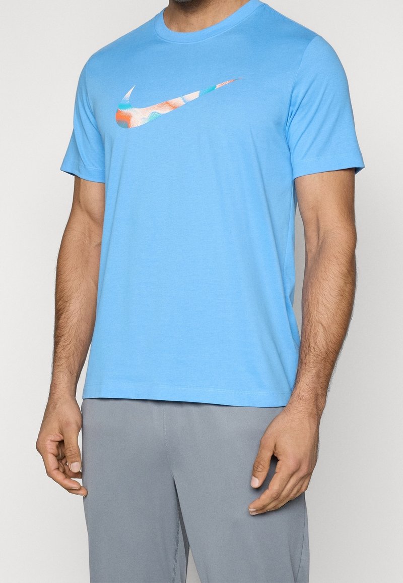 Vaaleansininen Nike-t-paita, jossa on pyöreä pääntie ja lyhyet hihat, sisältäen monivärisen swoosh-logon rinnoilla; sileä, teksturoitu kangas.