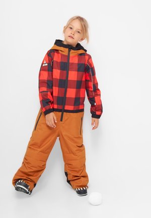Chaqueta de cuadros roja y negra con capucha marrón, combinada con pantalones de nieve color beige. Los pantalones tienen bolsillos laterales y detalles en negro. Hay una bola de nieve en el suelo.