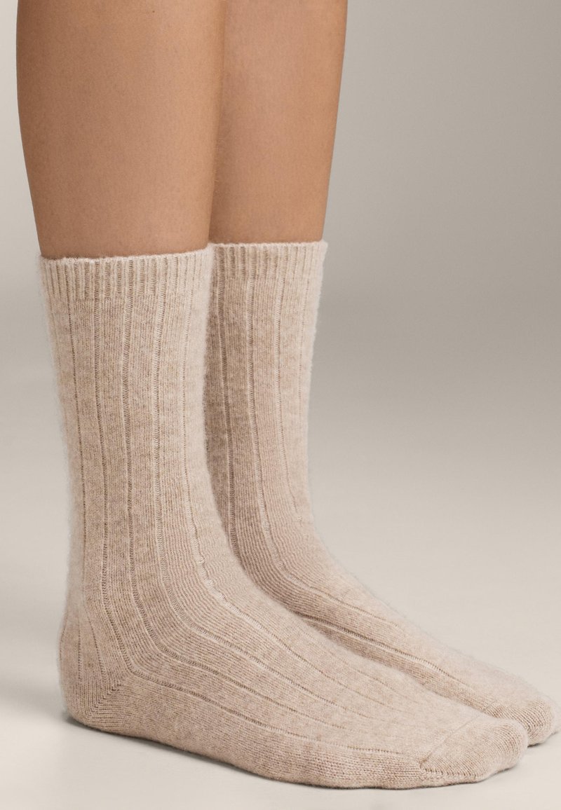 Calzini lavorati a maglia beige con texture a costine, lunghezza a metà polpaccio e design della punta senza cuciture. Materiale morbido simile alla lana con leggere variazioni di colore.