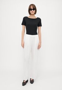 Top preto de mangas curtas, calças largas brancas, sapatos de salto grosso pretos e óculos de sol escuros. Texturas suaves e uma silhueta moderna.