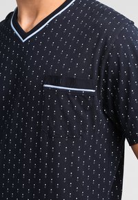 Marineblauwe T-shirt met korte mouwen en V-hals, voorzien van een wit stippenpatroon, een borstzak en een dunne lichtblauwe accent langs de halslijn.