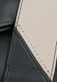 Schwarzes und beiges strukturiertes Leder mit kontrastierenden Nähten, das ein kantiges Design und sichtbare Nähte aufweist, die das Handwerk hervorheben.