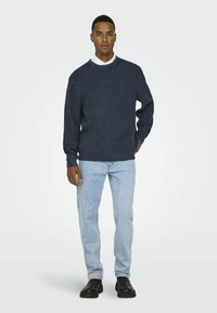 Donkerblauwe geribbelde gebreide trui met een ronde hals, gecombineerd met lichtblauwe denim jeans en zwarte schoenen, met een ontspannen fit.