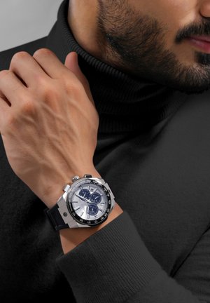 Chronograph watch with a silver dial, black bezel, and rubber strap. Features two subdials and stainless steel casing. Worn on a hand.