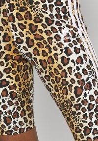 Leopardmönstrade shorts gjorda av mjukt tyg, med svarta, bruna och gula mönster, samt tre vita ränder p å sidan.