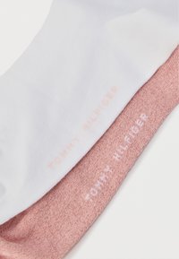 Δύο ζευγάρια κάλτσες: ένα λευκό και ένα ροζ. Και τα δύο έχουν ανάγλυφο κείμενο "TOMMY HILFIGER" σε αντίστοιχα χρώματα. Μαλακό, ελαστικό ύφασμα.