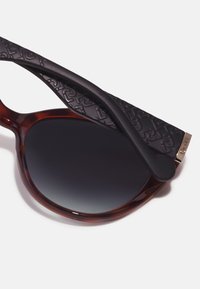 Gafas de sol con montura carey, patas negras texturizadas, lentes oscuros con degradado, y detalle en oro en el herraje de metal.