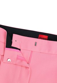 Pantaloni rosa con una texture liscia, dotati di un interno nero, chiusura con cerniera e un dettaglio in hardware argentato con etichetta logo.